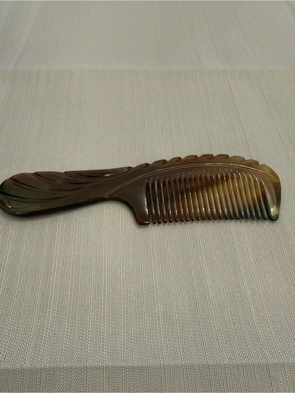 Natural ox horn hair comb featuring a curved,carved handle and fine teeth.